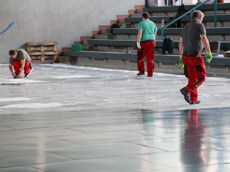 Monteure von ATHE-Therm in einer großen Halle bei der Installation einer Fußbodenheizung